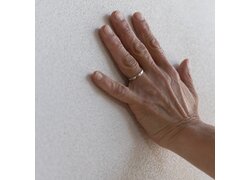 Hand berührt eine grob strukturierte, helle Putzwand.