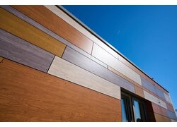 Bunte Fassadenverkleidung mit Holzoptik-Paneelen in verschiedenen Farbtönen, aufgenommen bei klarem, sonnigem Himmel.