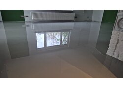 Glänzend versiegelter, grauer Boden in einem Wohnraum, in dem sich ein Fenster spiegelt.