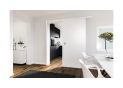 Helles modernes Interieur mit weißer Schiebetür, die eine schwarze Küche und minimalistisches Dekor freigibt