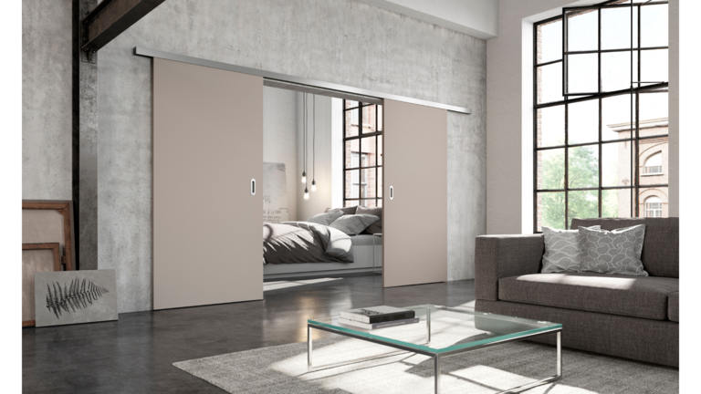 Industriell inspiriertes Wohnzimmer mit großen Fenstern, grauem Sofa und beigen Schiebetüren, die ein Schlafzimmer offenbaren