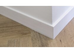 Weiße Sockelleiste an Wandecke über hellem Holzboden.