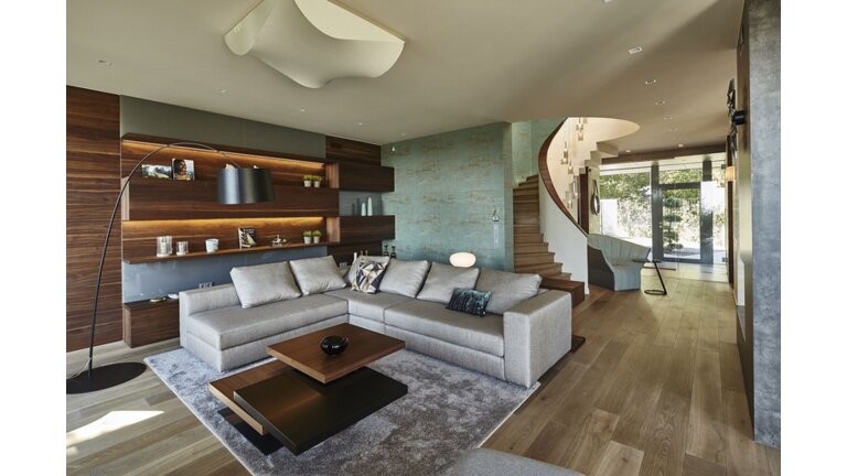 Modernes Wohnzimmer mit Holzboden, Sofa und geschwungener Treppe.