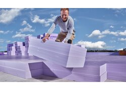 Ein Bauarbeiter beim verlegen fliederfarbener JACKODUR EVO XPS-Dämmstoffplatten welcher in die Kamera lächelt