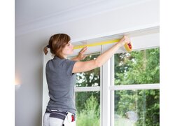  Person, die gelbes Abdeckband entlang des oberen Rahmens eines großen Fensters anbringt.