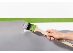 Hand streicht Wand mit Pinsel, Malerband schützt.