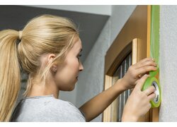 Frau klebt grünes Malerband an Türrahmen.