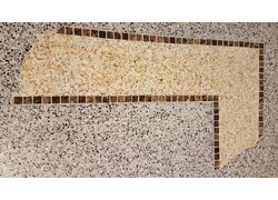 Nahaufnahme eines Lafina Terrazzo, hell mit dunkl bepunktetem Muster. In der Mitte ist ein Antik wirkendes L gelegt. Der Rand ist durch braune Mosaiksteine vom gewöhnlichen Terrazzo getrennt. Der Innere Terrazzo de L ist gelb mit gelb braunem Muster