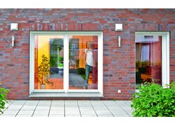 Außenansicht eines Ziegelhauses mit zwei installierten Leaf MEnV Lüftungsöffnungen oberhalb einer Terrassentür. 