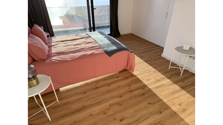 Modernes Schlafzimmer mit Holzoptik-Vinylboden, rosa Bett und weißen Möbeln.