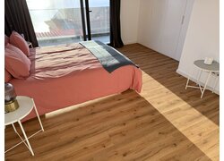 Modernes Schlafzimmer mit Holzoptik-Vinylboden, rosa Bett und weißen Möbeln.