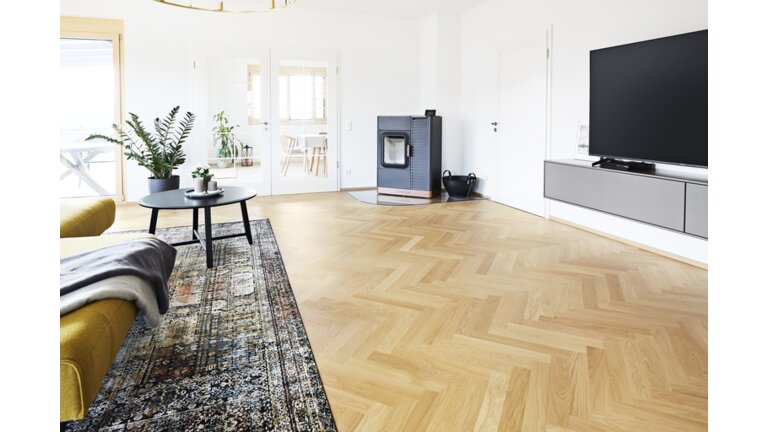 Zweischichtfertigparkett, Trägermaterial Birke Multiplex Helles Wohnzimmer mit Fischgrätparkett und Ofen.
