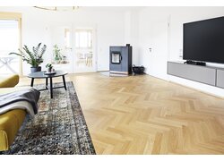 Zweischichtfertigparkett, Trägermaterial Birke Multiplex Helles Wohnzimmer mit Fischgrätparkett und Ofen.