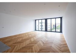 Großes Wohnzimmer mit Fischgrätparkett und Fensterfront.