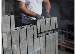 SEMBLA Mauerwerksystem, gestapelte Beton-Hohlblocksteine mit einem speziellen Verbindungsprofil für den Mauerbau, Handwerker mit Handschuhen stapelt die Betonsteine aufeinander