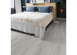 Schlafzimmer mit hellgrauem Holzboden, weißem Bett und blauen Kissen.
