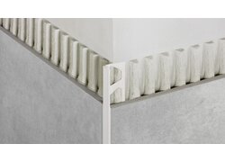 Das Bild zeigt eine Ecke, die mit einem Kantenschutzprofil in hellem Farbton versehen ist, das zwischen zwei gefliesten Flächen eingesetzt wurde, um eine saubere und geschützte Kante zu schaffen; es handelt sich um ein Produktbild für ein Kantenschutzprofil von Schlüter-Systems.