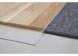 Ein Aluminiumprofil bildet die präzise und saubere Verbindung zwischen einer Holzoptik-Laminatfläche und ein grauer Teppich