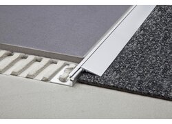  Nahaufnahme einer Bodenübergangsschiene aus Aluminium, die zwei unterschiedliche Bodenbeläge trennt.
