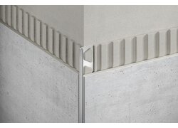 Bild zeigt eine Ecke, an der zwei verschiedene Texturoberflächen aufeinandertreffen, getrennt durch ein schlankes Edelstahlprofil.