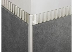 Bild zeigt eine Ecke, an der zwei verschiedene Texturoberflächen aufeinandertreffen, getrennt durch ein schlankes Edelstahlprofil.