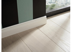 Sockelleiste weiß foliert, profiliert und schließt an gestreifte Wand und hellem Holzboden an.