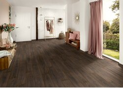 Heller Raum mit dunklem Holzboden, weißen Wänden, Möbeln und Gardine, die auf einen Garten blicken.