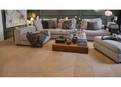 mafi Naturholzboden Eiche in einem Wohnzimmer. man sieht ein großes Sofa, davor ein Couchtisch und dahinter eine mit Holz verkleidete Wand in grün. Auf dem Tisch stehen Magnolienäste mit Blüten