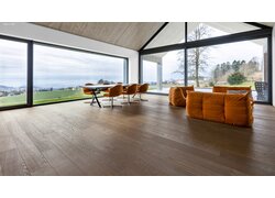 mafi Naturholzboden Eiche in einem großen Besprechungsraum. Die Wände sind nahezu komplett verglast womit man ins Freie sieht. Der Raum liegt auf einem Hügel. Es gibt einen Tisch mit Stühlen und zwei Sofas, passend zum Boden