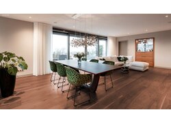 Dunkler mafi Naturholzboden Nuss in einem großen Wohn- Essbereich mit Esstisch, Stühlen, Sofa und Vitrine. Mittig dahinter Fenster und Türen welche auf eine Terrasse führen