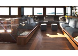 Dunkler mafi Naturholzboden Nuss in einem großen Aufenthaltsbereich. Man sieht eine helle Sitzecke mit einer großen Fensterreihe dahinter und Sicht in die Berge