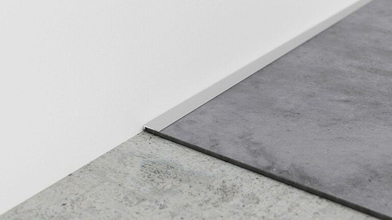 Metallkante trennt zwei Bodenbeläge an Wand