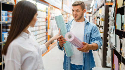 Zweite Wahl im Handel Junges Pärchen steht im Baumarkt und sieht sich zwei verschiedene Tapeten an